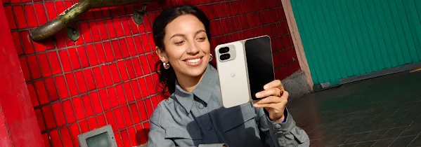 一个人面带微笑，看着手中的浅陶米色 Pixel 9 Pro Fold。背景是红色砖墙。